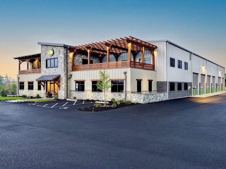 A large commercial building with a stone and metal exterior. The building includes a second-floor patio with wooden pergola accents and multiple garage bays on the side.