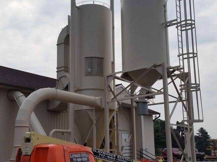 industrial silos with an orange lift parked nearby during the painting process.