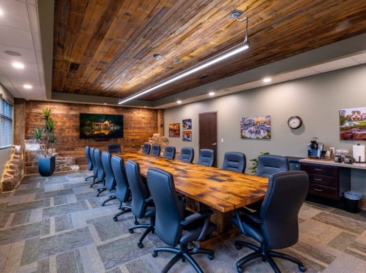 A well-lit conference room featuring a long wooden table with leather chairs and a rustic wood ceiling. The room has a modern design with a warm and professional atmosphere