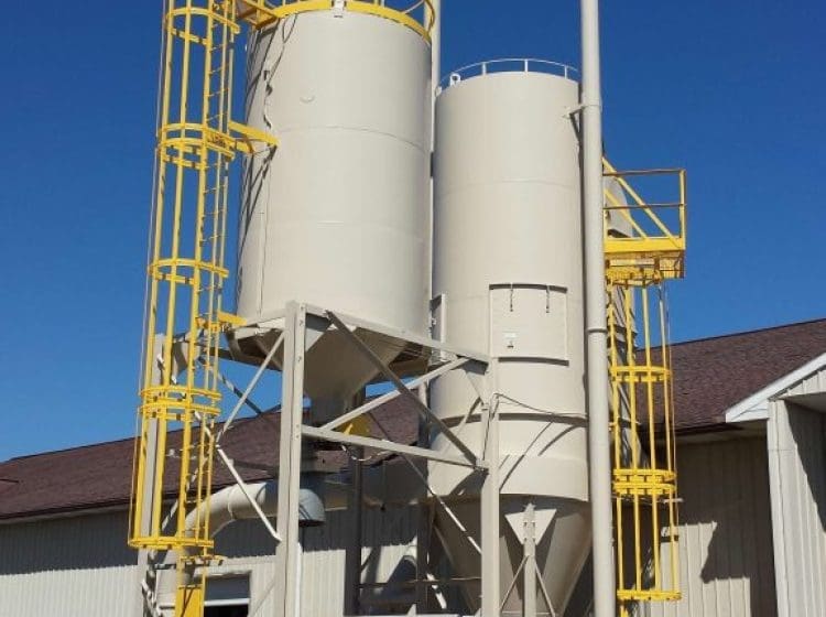 Freshly painted industrial silos with yellow safety ladders and platforms outside a facility.