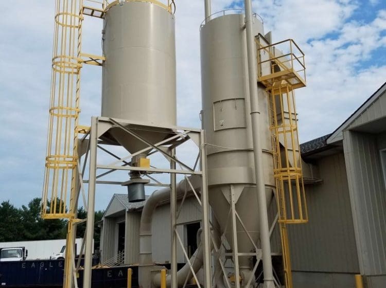Two industrial silos with visible piping, yellow ladders, and maintenance equipment nearby.