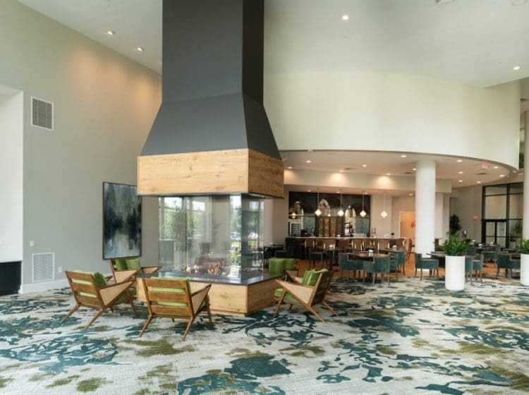 Sophisticated lounge area featuring a large central fireplace, modern wood accents, and mid-century style chairs. The room opens into a dining space, creating a relaxed yet stylish environment