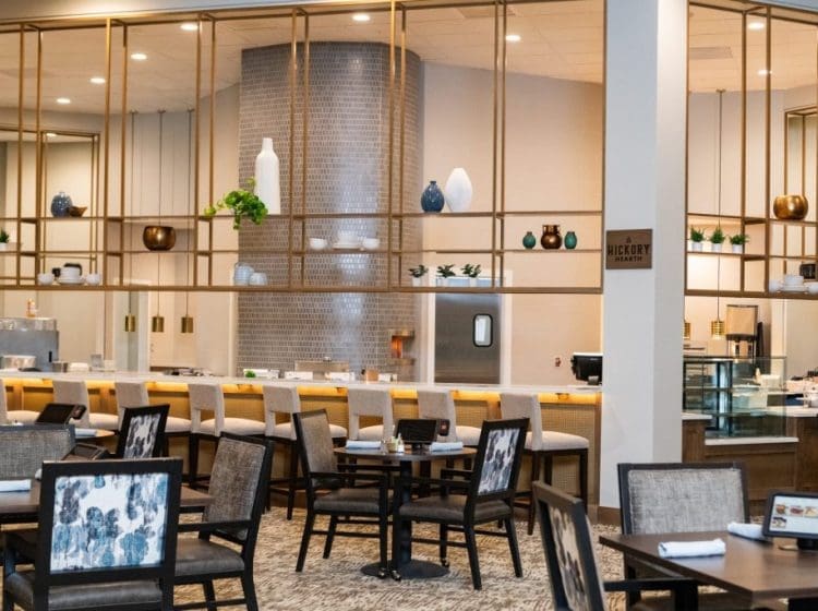 Chic dining space with a sleek open kitchen and decorative shelving. The room features comfortable seating, a variety of plants, and modern lighting