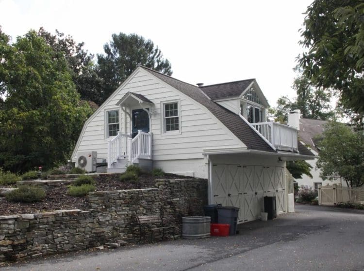 Detached residential garage with white siding and stone retaining wall, surrounded by landscaping.