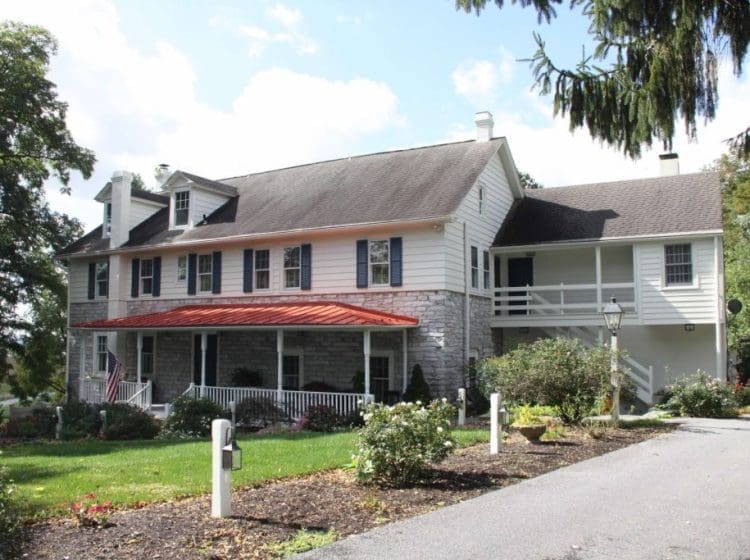 Large two-story house with a mix of stone and siding, featuring a red metal roof over the front porch.