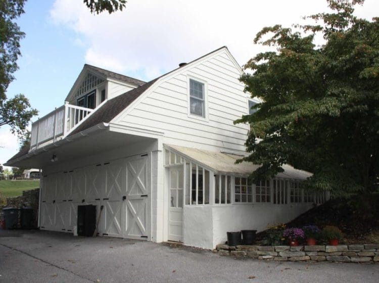 Side view of a two-story garage with white siding, a balcony, and a small greenhouse addition.