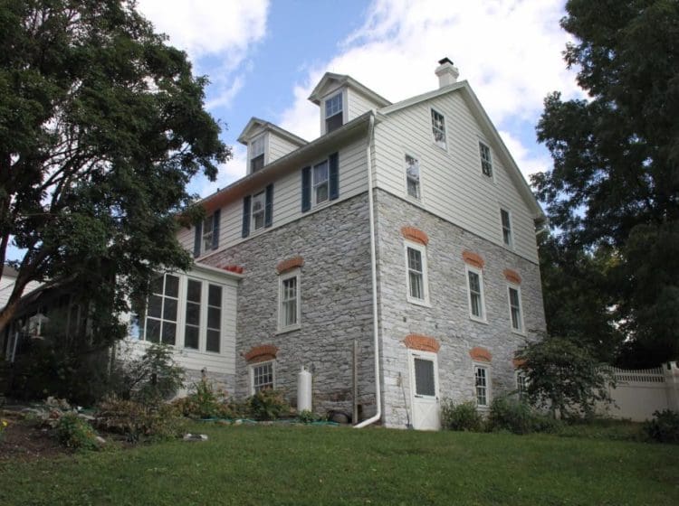 Rear view of a house with stone walls and white siding, surrounded by a landscaped backyard.