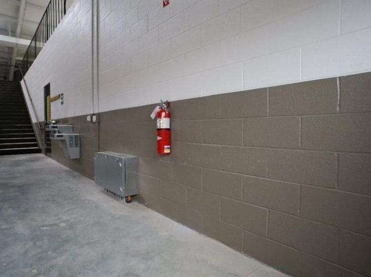 Industrial facility with a two-tone acrylic drywall finish. Fire extinguisher mounted on the wall. Staircase visible in the background