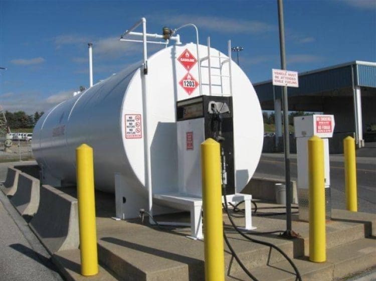 White gasoline storage tank with protective yellow bollards and attached fuel dispenser.