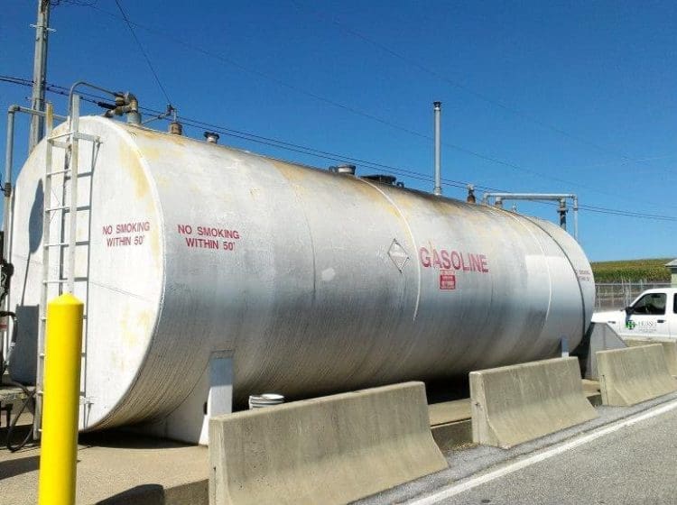 Large industrial gasoline tank with concrete barriers and attached fueling station.