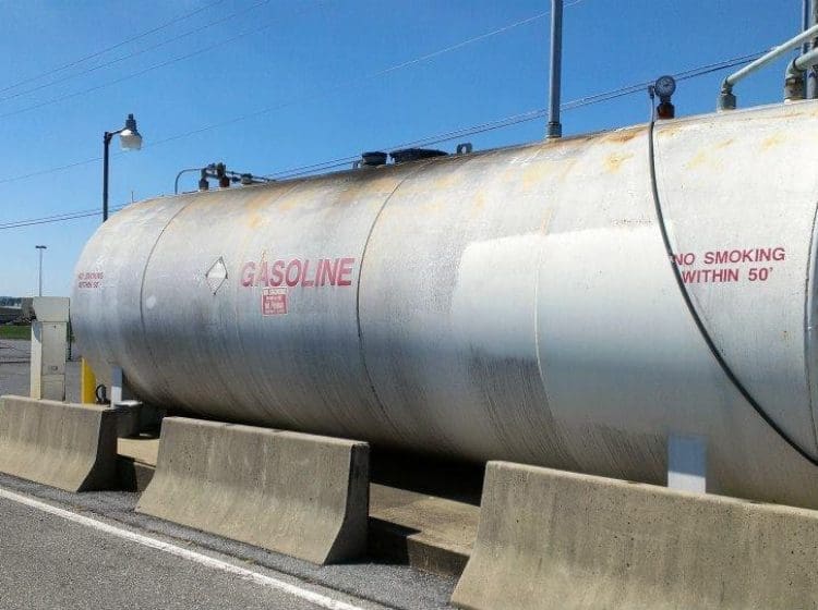 Close-up view of a weathered gasoline tank with warning signs and flammable markings.
