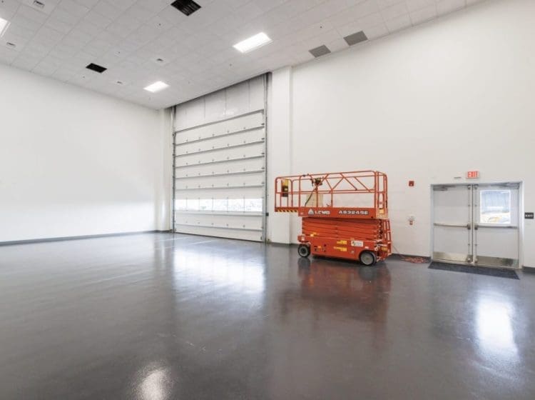 Spacious industrial room with a scissor lift and a large overhead garage door.