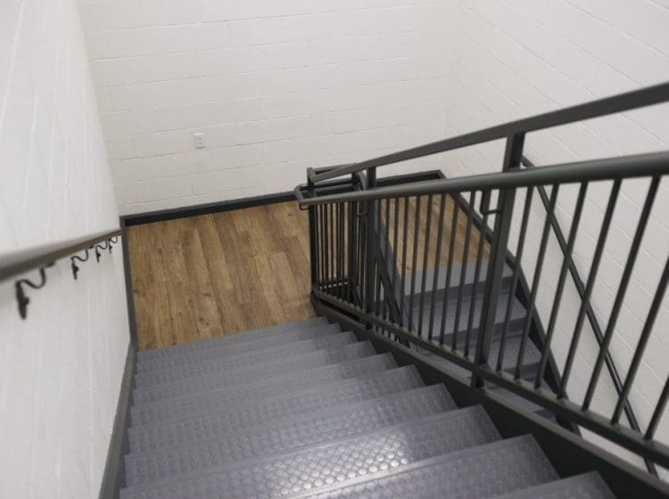 Interior stairwell with black metal railings and wood-look flooring at the base.