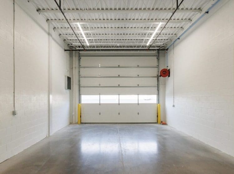 Clean industrial garage with white walls, an overhead garage door, and polished concrete floors.