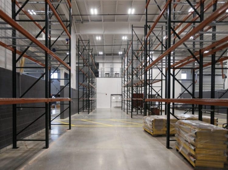 Industrial warehouse with tall metal shelving racks and pallets of materials.