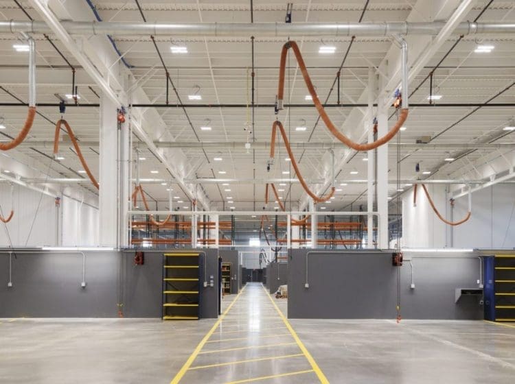 Industrial warehouse with overhead ventilation systems, yellow-lined pathways, and storage shelves.