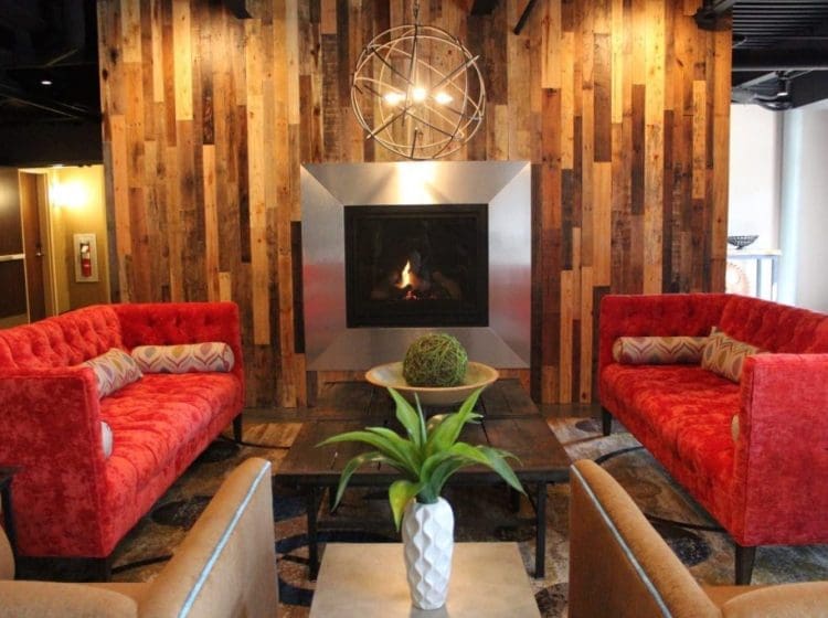 A modern lobby with red sofas, a wooden accent wall, and a fireplace as a focal point.