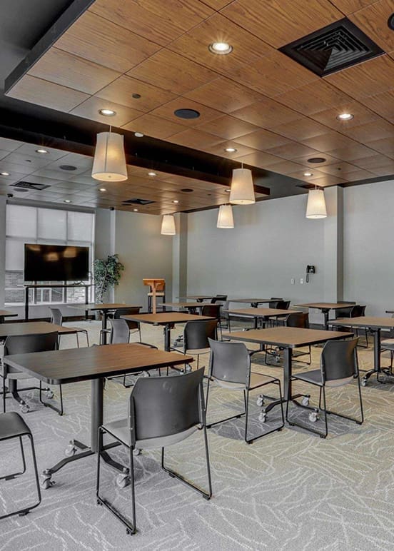 A professional conference room with wooden ceiling panels, pendant lighting, and multiple tables and chairs arranged for meetings.