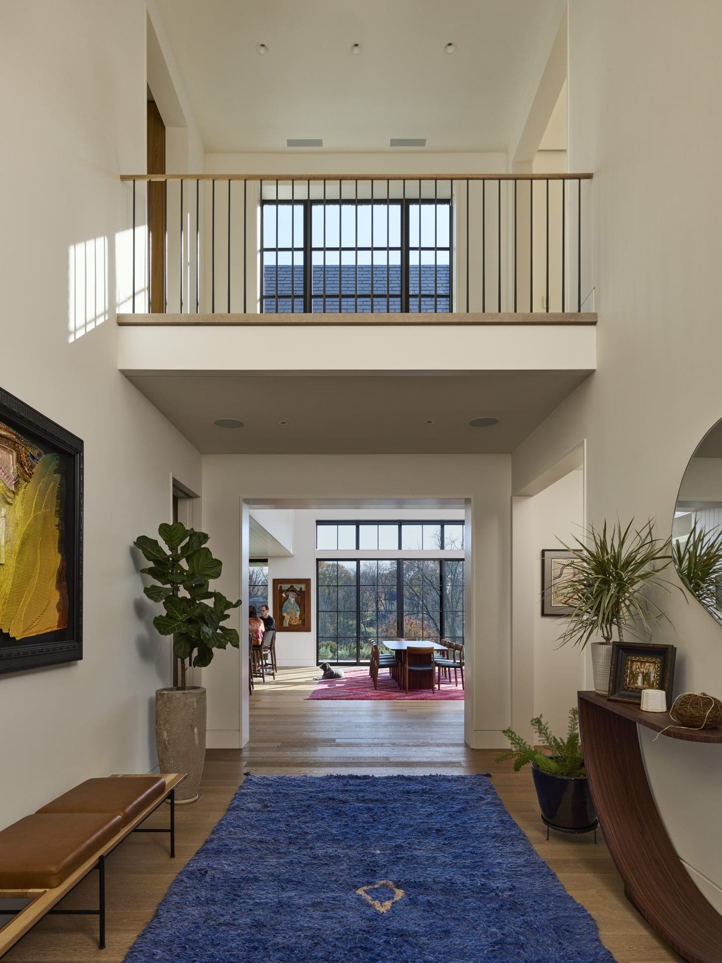 A spacious entry hallway featuring a blue rug, modern decor, a tall plant, and a view into a dining area with large windows.