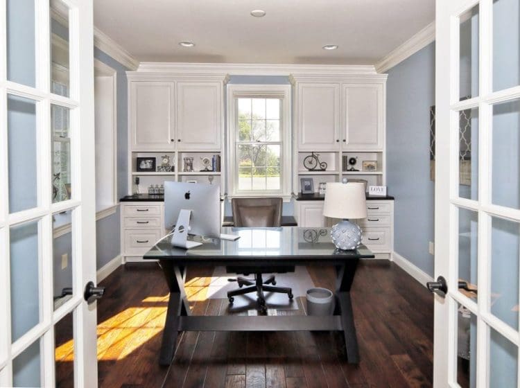 A bright home office with blue walls, white cabinets, and a modern desk with a computer.