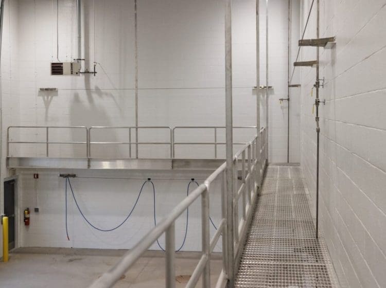 Industrial interior with a high ceiling, white walls, and a suspended metal walkway with railings.