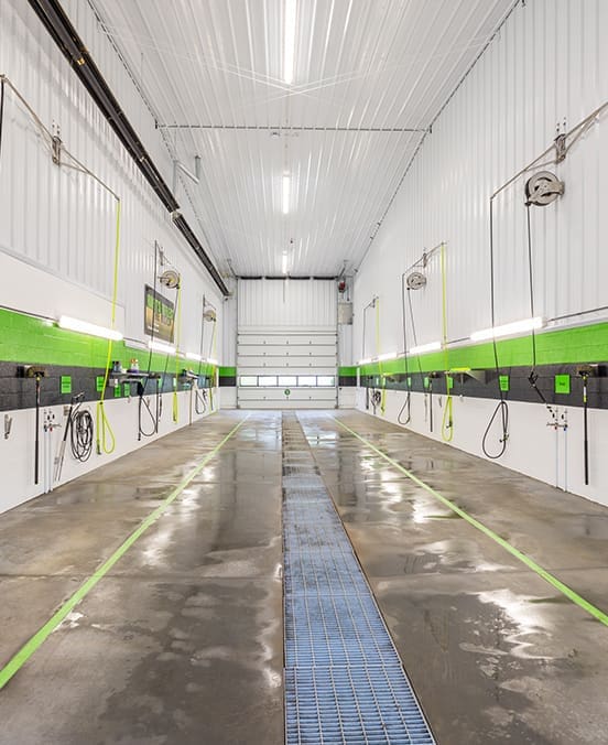 A bright and modern car wash bay with white walls, green accents, and stainless steel equipment.