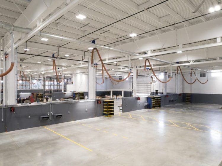 Spacious industrial workspace with overhead piping, workstations, and a polished concrete floor.