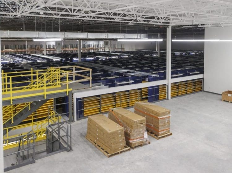 Industrial warehouse with stacked shelving units, a yellow staircase, and organized materials on pallets.